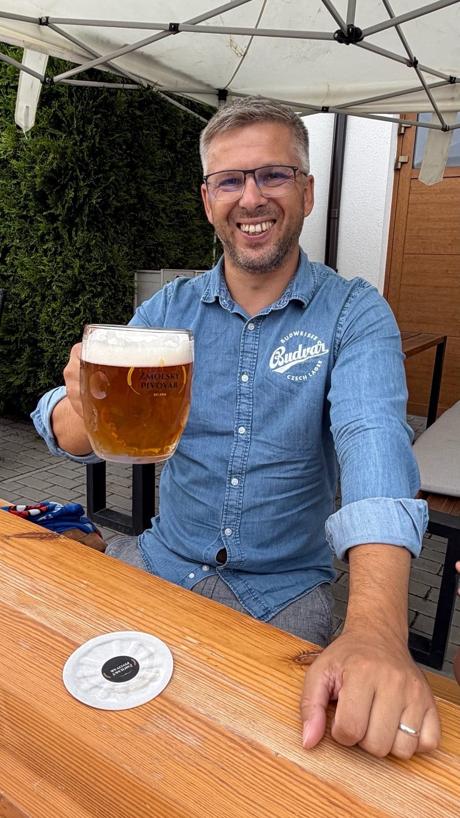 Průvodce Beerasmu s půllitrem piva na zahrádce pivovaru